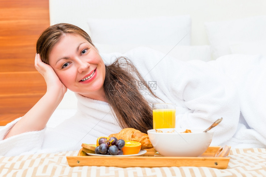 快乐的美丽女孩在床上带着一盘食物图片
