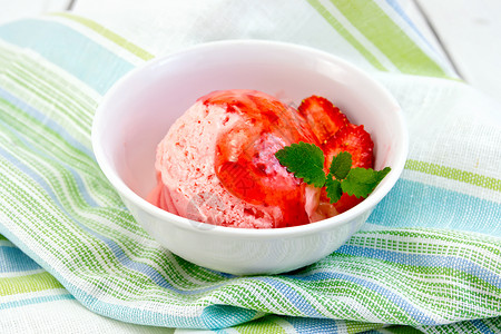 在碗中的冰淇淋白碗中的草莓冰淇淋和糖浆在木板背景的条纹布纸巾上背景