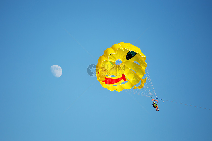 一艘降落伞在海上被拖走背面是蓝色的天空左边是月亮图片