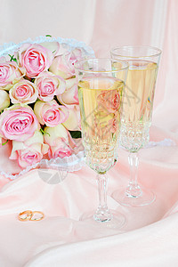 粉红玫瑰花束瓶粉红玫瑰结婚戒指和两杯白葡萄酒的花束结婚戒指和两杯白葡萄酒背景