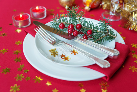 银刀叉餐盘胡利浆果松树枝和燃烧的蜡烛放在一张桌子上面有红色桌布图片