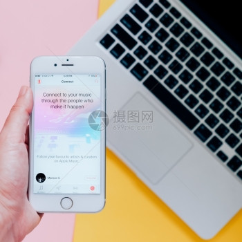 2016年月8日手持苹果iphone6显示苹果音乐应用程序并带有笔记本电脑背景苹果音乐是新推出的ibones音乐流服务图片
