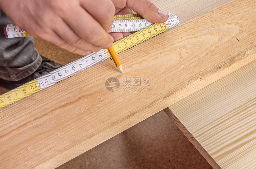 木质板测量的手用一个拿着测量胶带的人手对着木质板并用铅笔打上标记图片