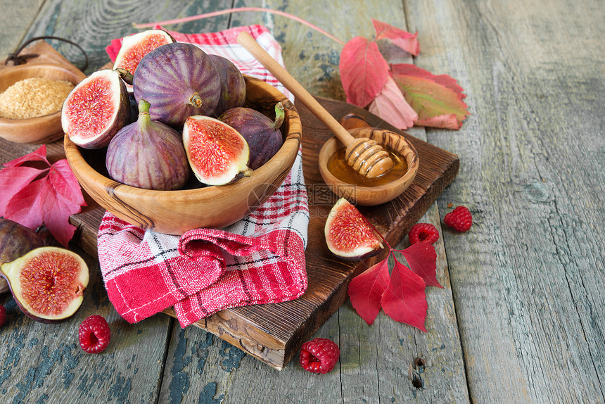 木碗红草莓甘蔗糖蜂蜜中的成熟无花果旧切割板上的餐巾纸和秋叶都躺在旧木桌上图片