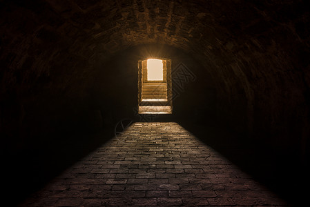 中世纪欧洲地下室内部有圆天花板和石地入口处有强烈的太阳灯背景图片