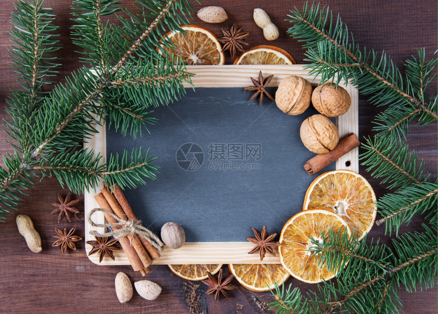 圣诞节背景空白黑板周围环绕着绿色圆形树枝和各种香料坚果和干橙子图片