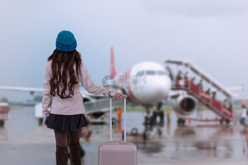 身穿毛衣带行李的蓝纱帽在机场等待旅行者度假游概念的亚洲行妇女图片