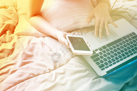 特写女人懒洋洋地躺在床上拿着笔记本电脑和智能手机色彩过渡风格和渐变色图片
