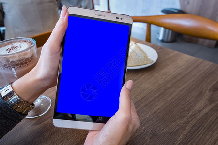 咖啡厅宣传折页手握机平板和蓝色屏幕的妇女手握机平板用于广告短信或宣传内容在咖啡厅的手机上宣读新闻背景