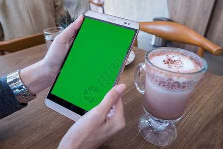 咖啡厅宣传折页手持机的妇女带有绿色屏幕用于广告短信或宣传内容在咖啡厅用手机阅读新闻背景