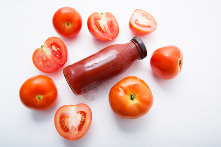 瓶装鲜番茄汁和白木底的鲜番茄片背景图片