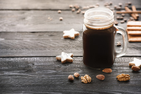 大玻璃罐装满热咖啡周围是肉桂星饼干胡桃和杏仁在一个生锈的黑木制桌子上在晨光下罐子高清图片素材