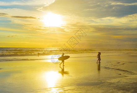 日落时在海滩上与冲浪板散步的者图片