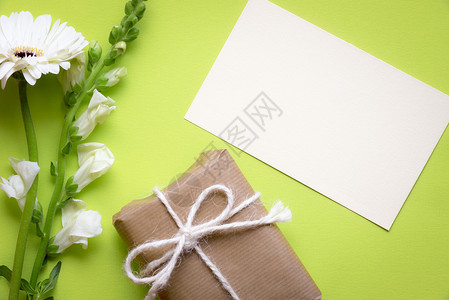 一朵白花礼物贴纸条的贺卡想法上面贴着白花和礼品盒包着棕色纸绑麻绳和弓并印在绿色背景上背景