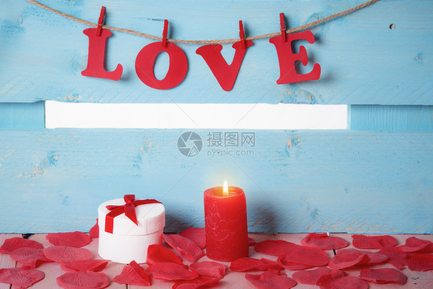 带着绑弓和红蜡烛的可爱白色礼物盒四周都是肥皂玫瑰花瓣和用红纸字母拼成的爱绑在绳子上图片