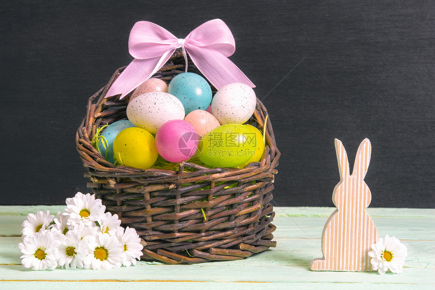 满是多色东方鸡蛋和粉弓的螺旋篮子周围着白菊花和木兔在一张桌子和堵黑墙上图片