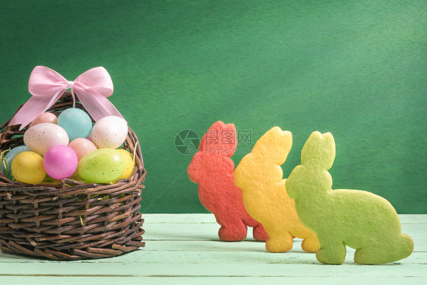 东面的横幅设计装满彩色蛋带丝结和三只兔子形状的饼干绿色背景图片