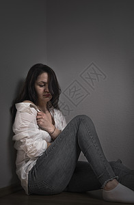 年轻女子情绪低落拉着衬衫遮盖自己坐在地板上靠墙背景图片