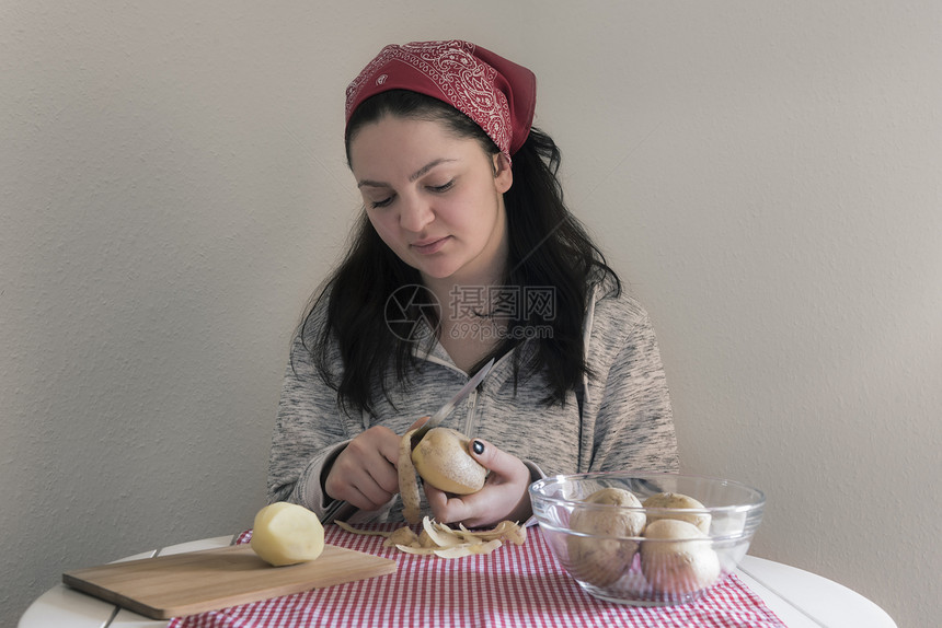 黑发女人在白天桌子上剥土豆准备一顿饭图片
