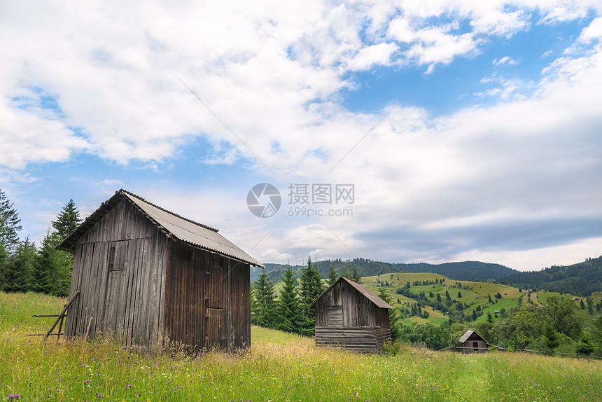 在罗马尼亚州萨达诺瓦附近的喀尔巴阡山脉里在一片充满野花的绿草地中间连续用木制谷仓进行生锈的布景图片