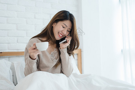 年轻女在床上享受热咖啡在卧室电话交谈图片