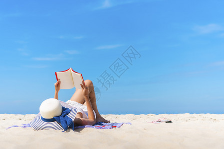 暑假旅行概念年轻女子在热带沙滩上蓝天躺着看书高清图片
