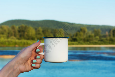 女人拿着白色的营火尼玛尔杯子模型夏季河景空的杯子模型设计宣传图片