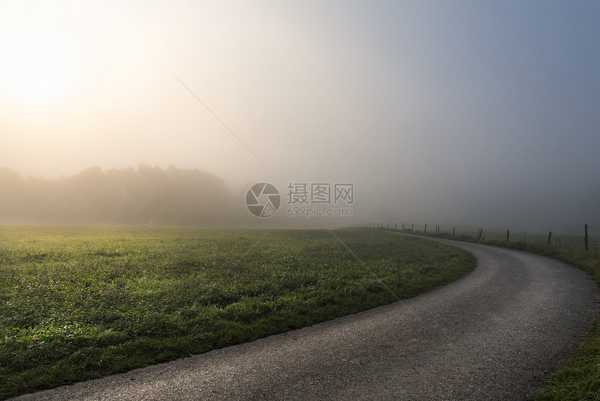 清晨的阳光穿透了迷雾照亮一片绿草原和条乡间公路在斯瓦比什大厅附近德国图片