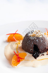 巧克力甜点巧克力味熔岩蛋糕香草酱柑橘白盘上的金叶子背景图片