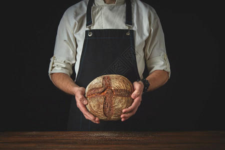 围裙里的面包师将握在黑色背景的手中men手握面包高清图片