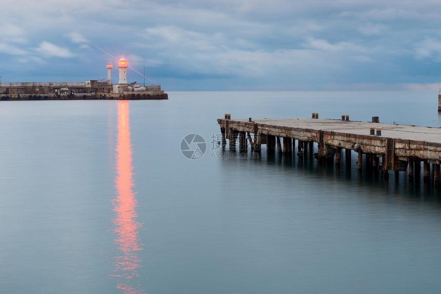 海岸灯塔的明光照亮日落时就在码头的架子上图片