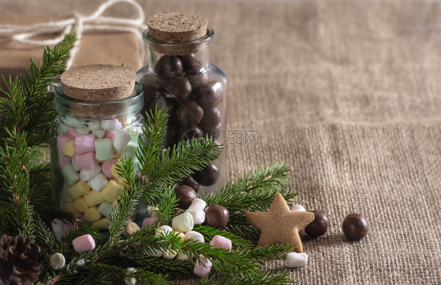 圣诞甜食环境有多彩的迷你棉花糖和巧克力果在瓶子里长青的树枝星形饼干在黄麻布料上图片