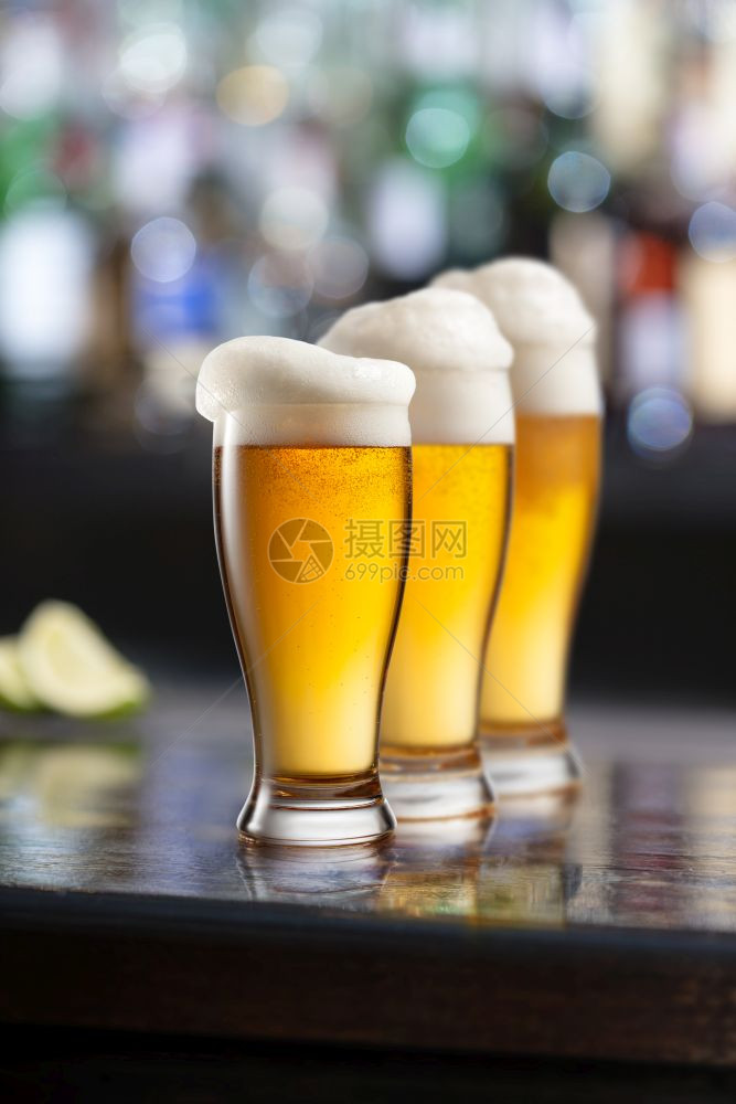 三杯轻啤酒配有泡沫的三杯轻啤酒放在木制桌子上图片