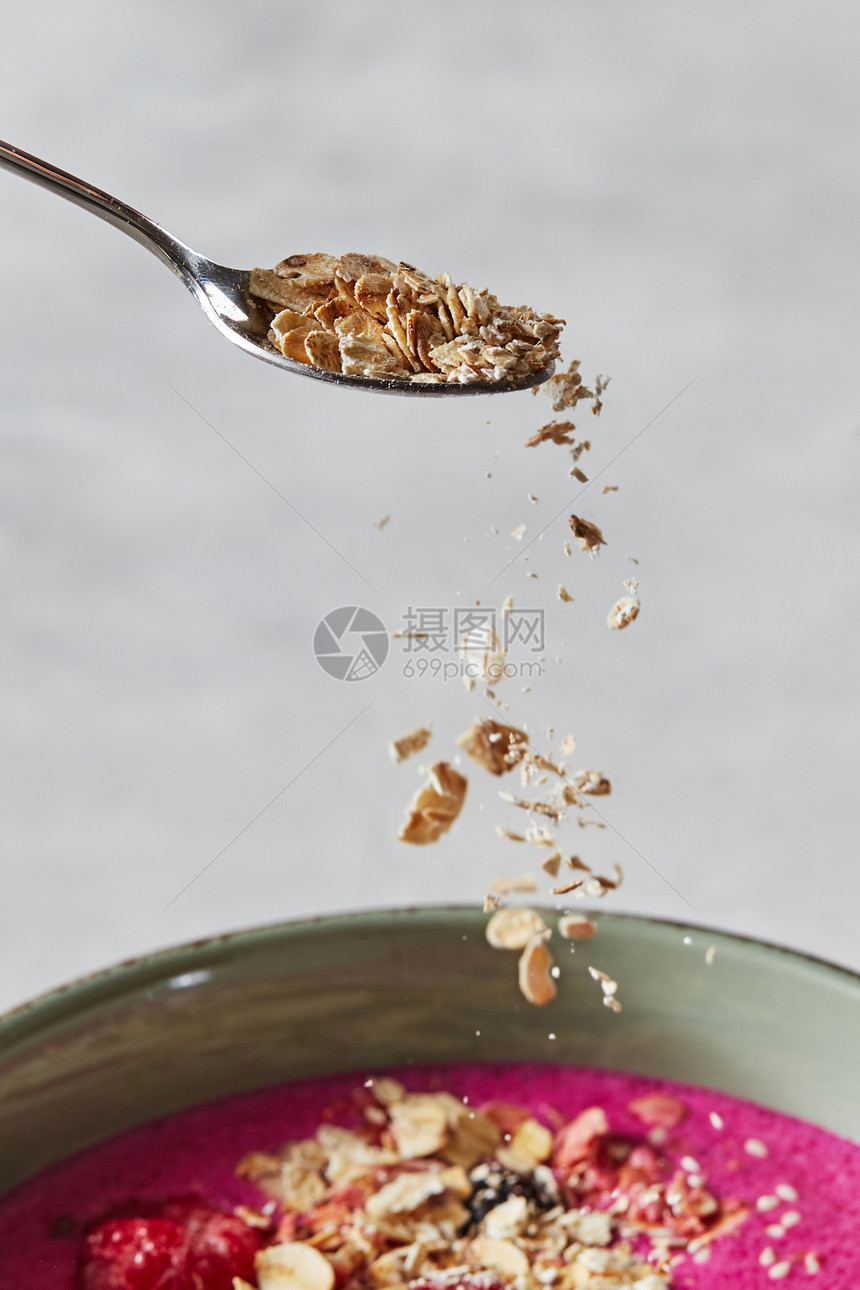 燕麦片从勺子上倒到盘碗里有新鲜果汁准备健康早餐燕麦片从勺子上倒到盘混凝土背景的梨子上在红沙倒图片