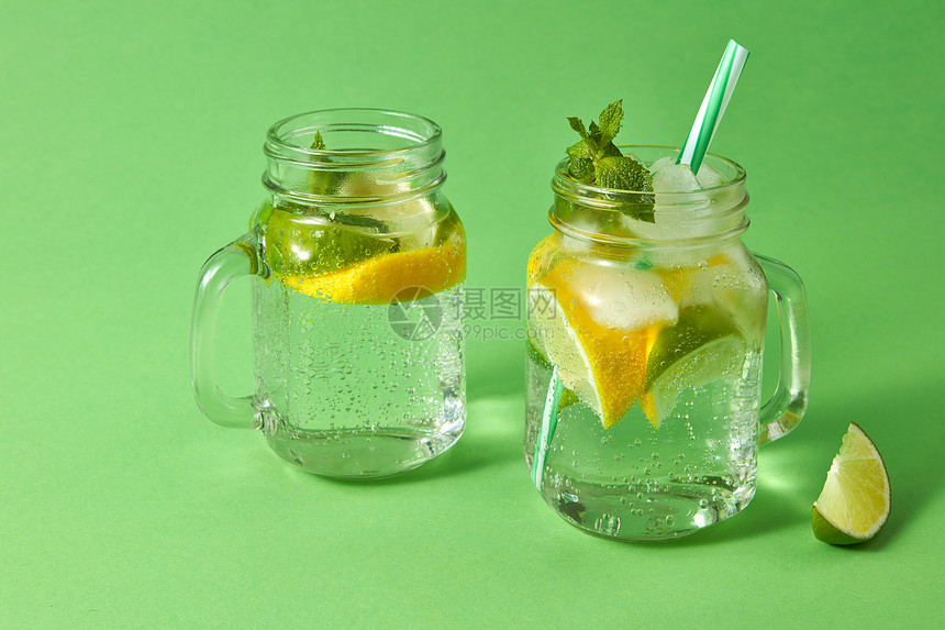 柠檬和冰水绿底玻璃中的塑料吸管柑橘水果片绿色底料上的夏季清新饮料玻璃罐中的自制火花鸡尾酒冷精或非夏季饮料的概念图片