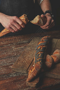 男人和手握被分割的袋式面包在深木背景上半径男手打破了袋式面包板图片