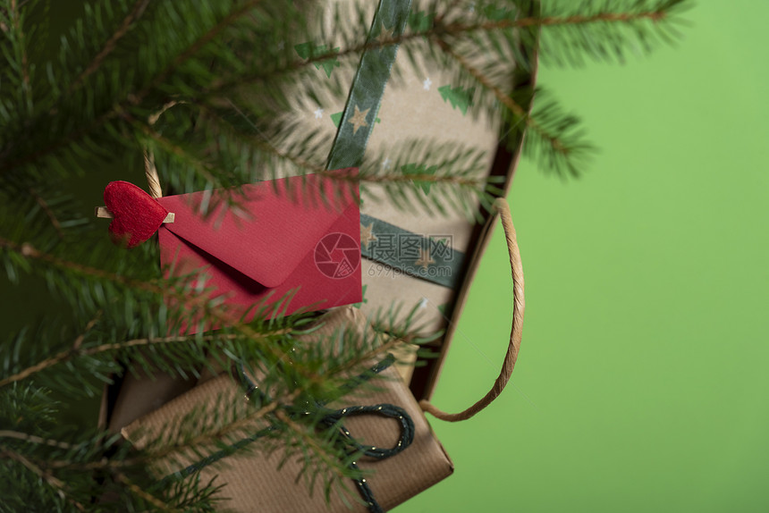 满纸袋的圣诞礼物放在松树枝下红色信封夹着一个红袋柄上有一个心脏形状的剪片图片