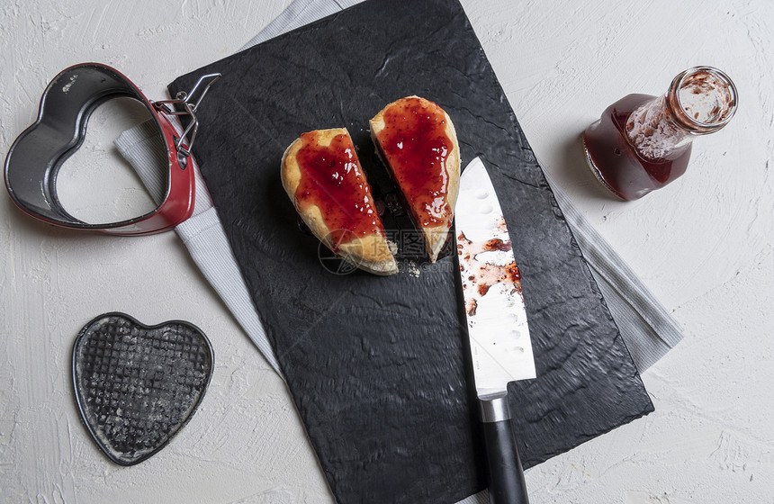 美味的自制心形红莓蛋糕在切菜板上成两片草莓酱倒在蛋糕上直接厨房的桌子上方图片