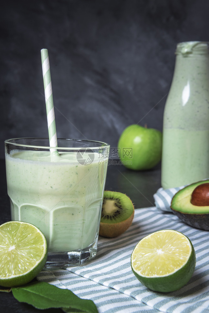 杯子里的绿色冰淇淋四周是石灰木薯鳄梨和苹果在厨房桌上有毛巾健康的生活方式概念脱毒饮料图片