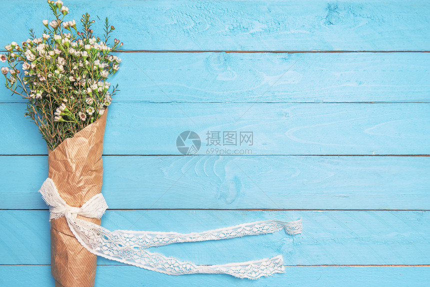 白春花束带丝捆绑的弓用旧纸包着放在一个空白的蓝色桌面上平板复制空间妇女日框图片