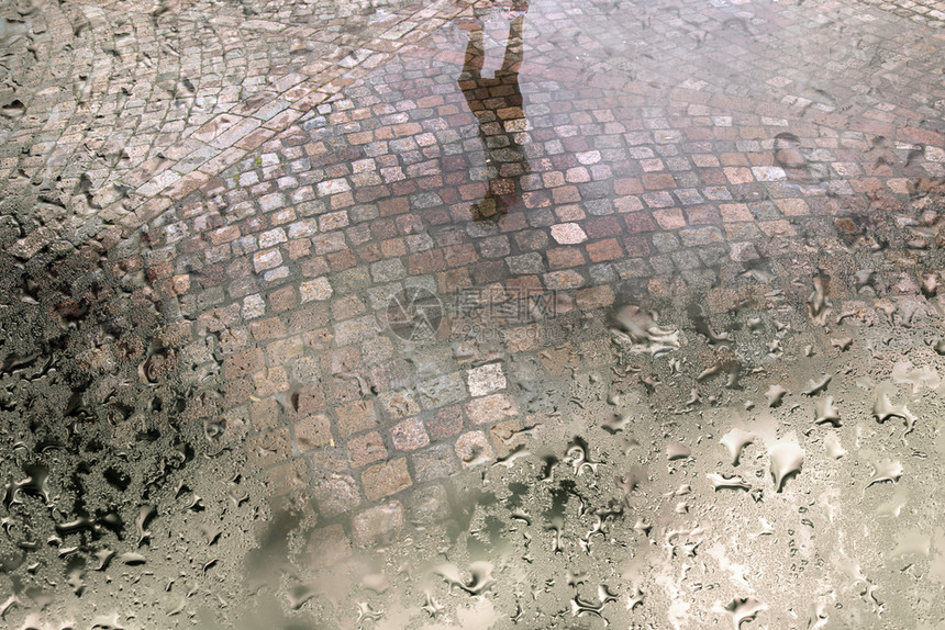 透过湿窗面看到雨水后街上人们的反光与可腐石头和水坑图片