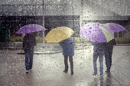 蒙蒙细雨4个人在多彩的雨伞和通过窗口看到满是雨滴的背景