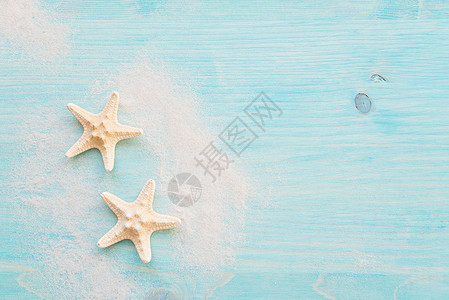 两个海星和白沙处于蓝色淡木甲板的背景背景图片