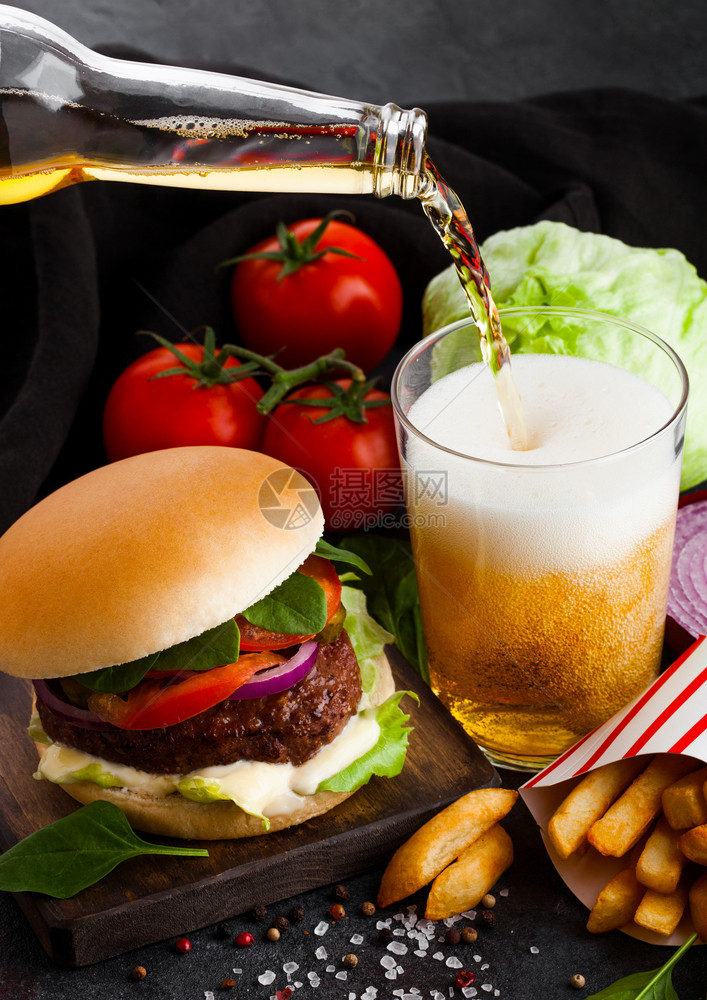 新鲜牛肉汉堡配有酱汁和蔬菜啤酒杯薯条在石器厨房背景图片