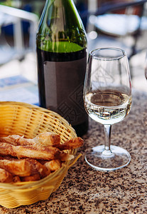 玻璃中的白葡萄酒皮诺石桌上的木篮中带有格里希尼面包棍图片