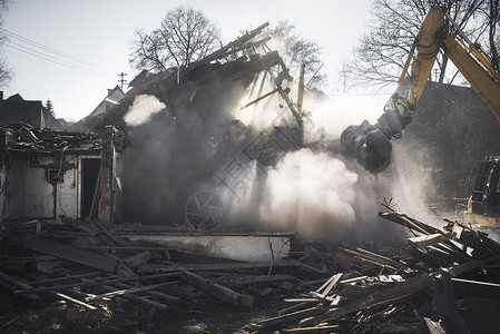 拆除一座用挖土机的老德国人房屋在灰尘云和阳光下坠毁建筑工地图片