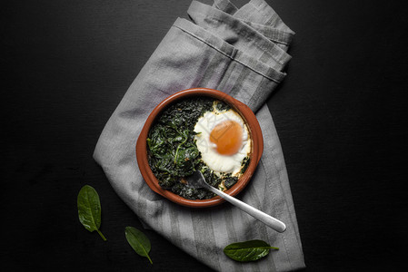 灰色台布背景含菠菜和鸡蛋的黏土锅俯视图背景图片