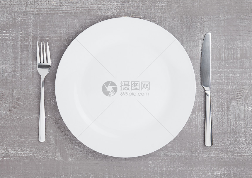 木板背景上带叉子和刀的白圆盘图片
