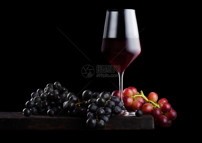 黑色背景的木板上盛着深红葡萄的酒图片