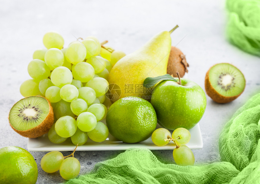 白陶瓷广场板上的新鲜有机绿色果实石器厨房背景梨和葡萄有石灰和苹果图片